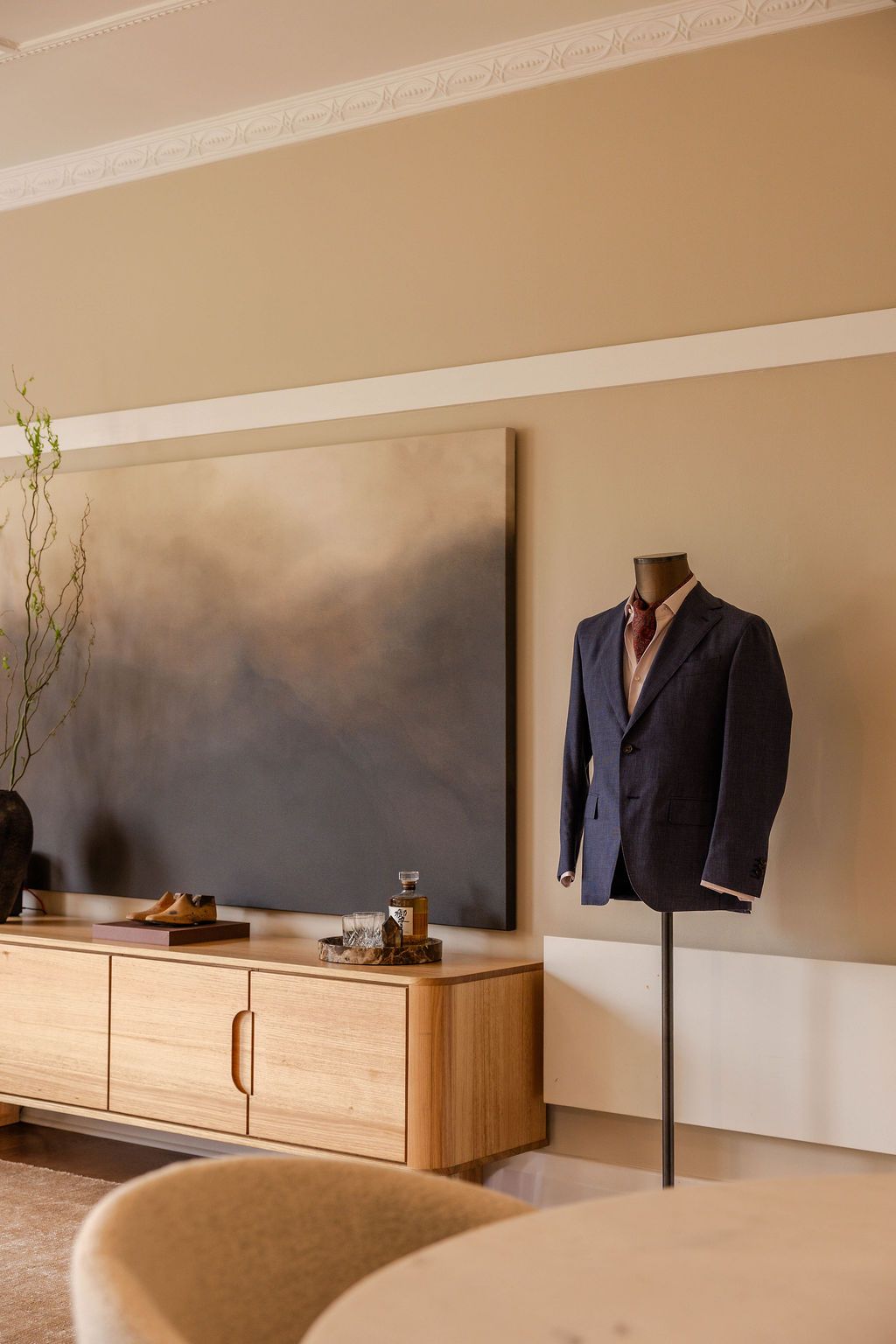A suited mannequin displayed alongside a beautiful wooden unit with an antique shoe mould & whisky resting on top